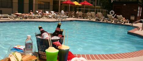 Zona junto a la piscina con sillones de descanso, sombrillas y una mesa con comida y bebidas.