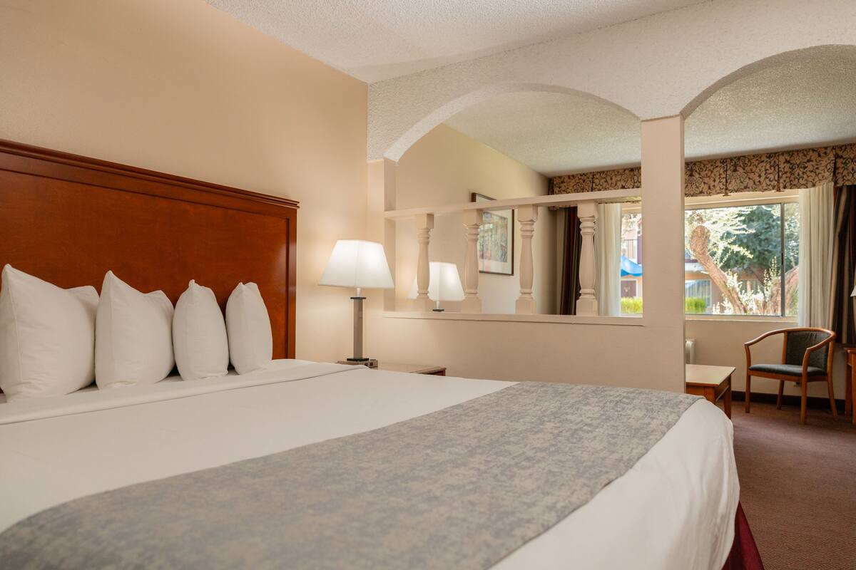 A hotel room with a large bed, a desk, a chair, and a window with curtains.