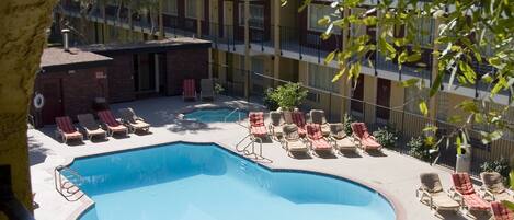 A swimming pool with sun loungers and umbrellas, surrounded by a building with multiple balconies.