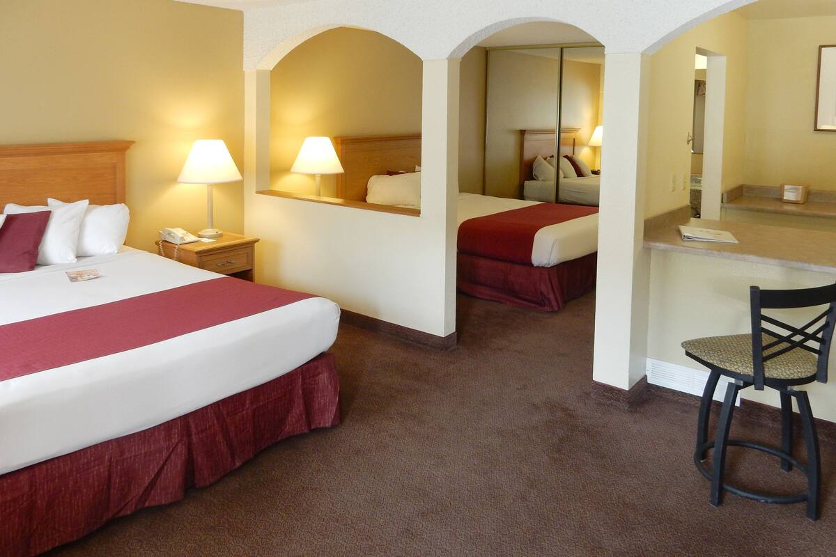 A hotel room with two beds, a desk, a chair, and a mirror.