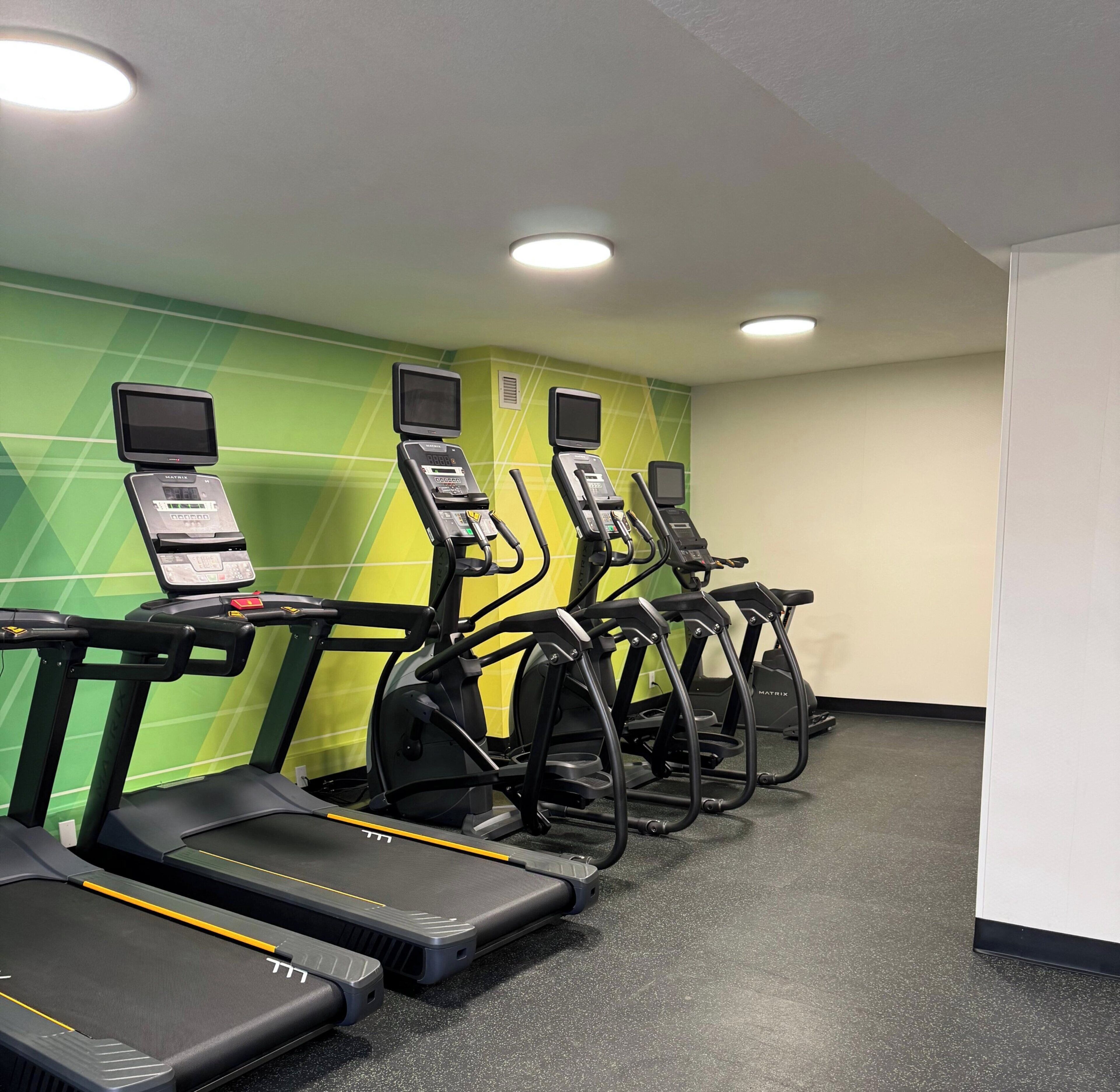 Zona de fitness amb esteves i màquines elíptiques, equipada amb pantalles digitals i panells de control.