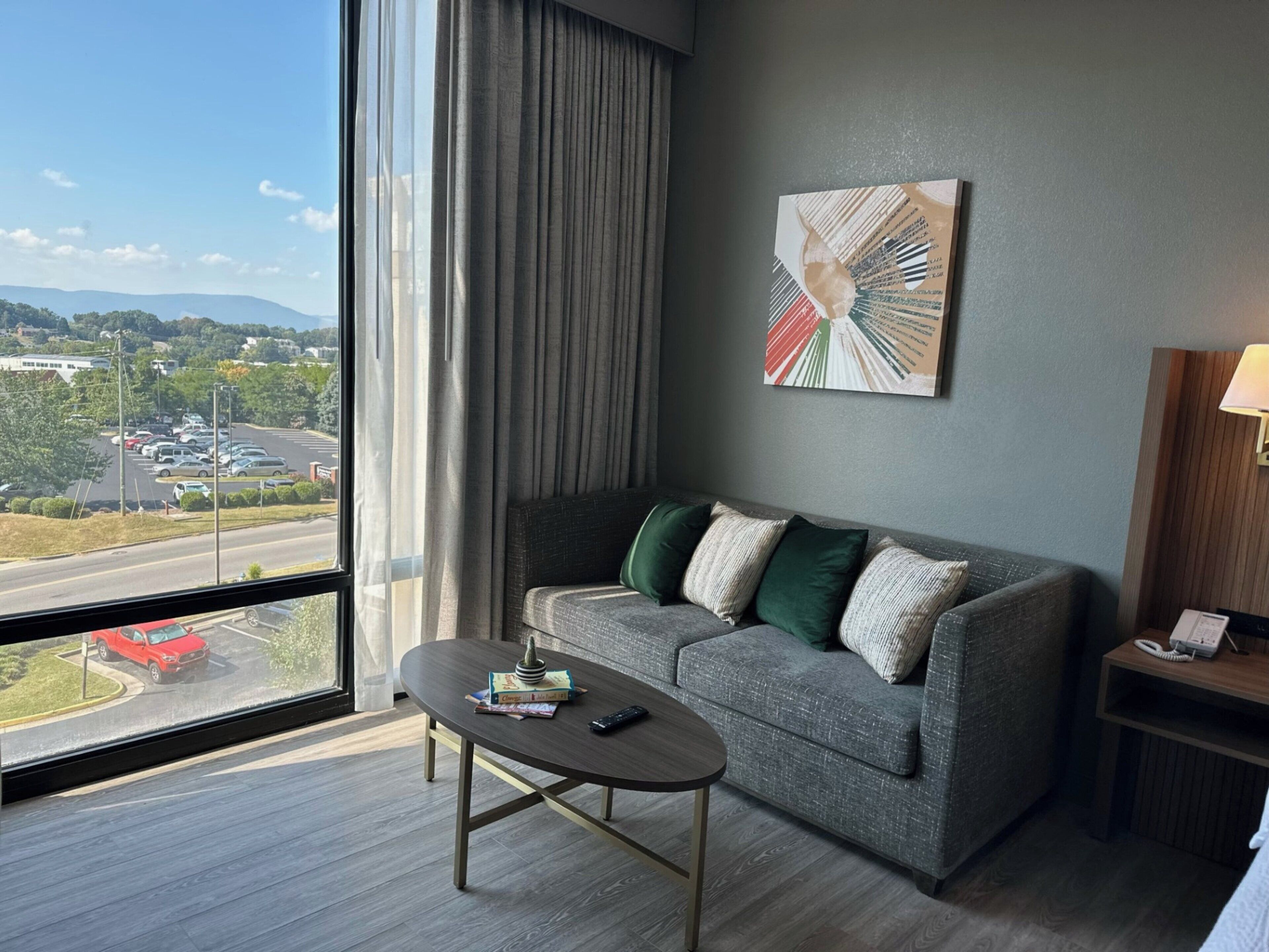 A hotel room with a gray sofa, a small table, a lamp, and a painting on the wall.