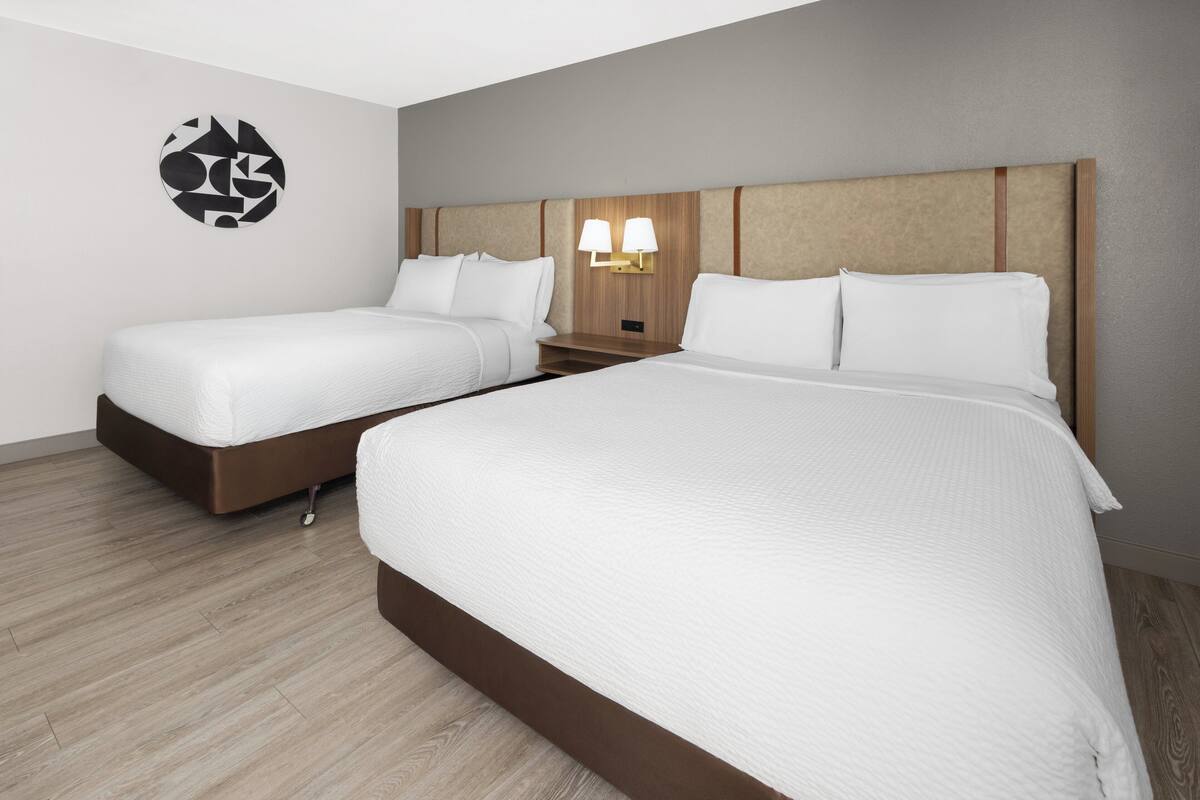 Une chambre d’hôtel avec deux lits, une tête de lit en bois, un luminaire fixé au mur et une œuvre d’art murale de forme circulaire.