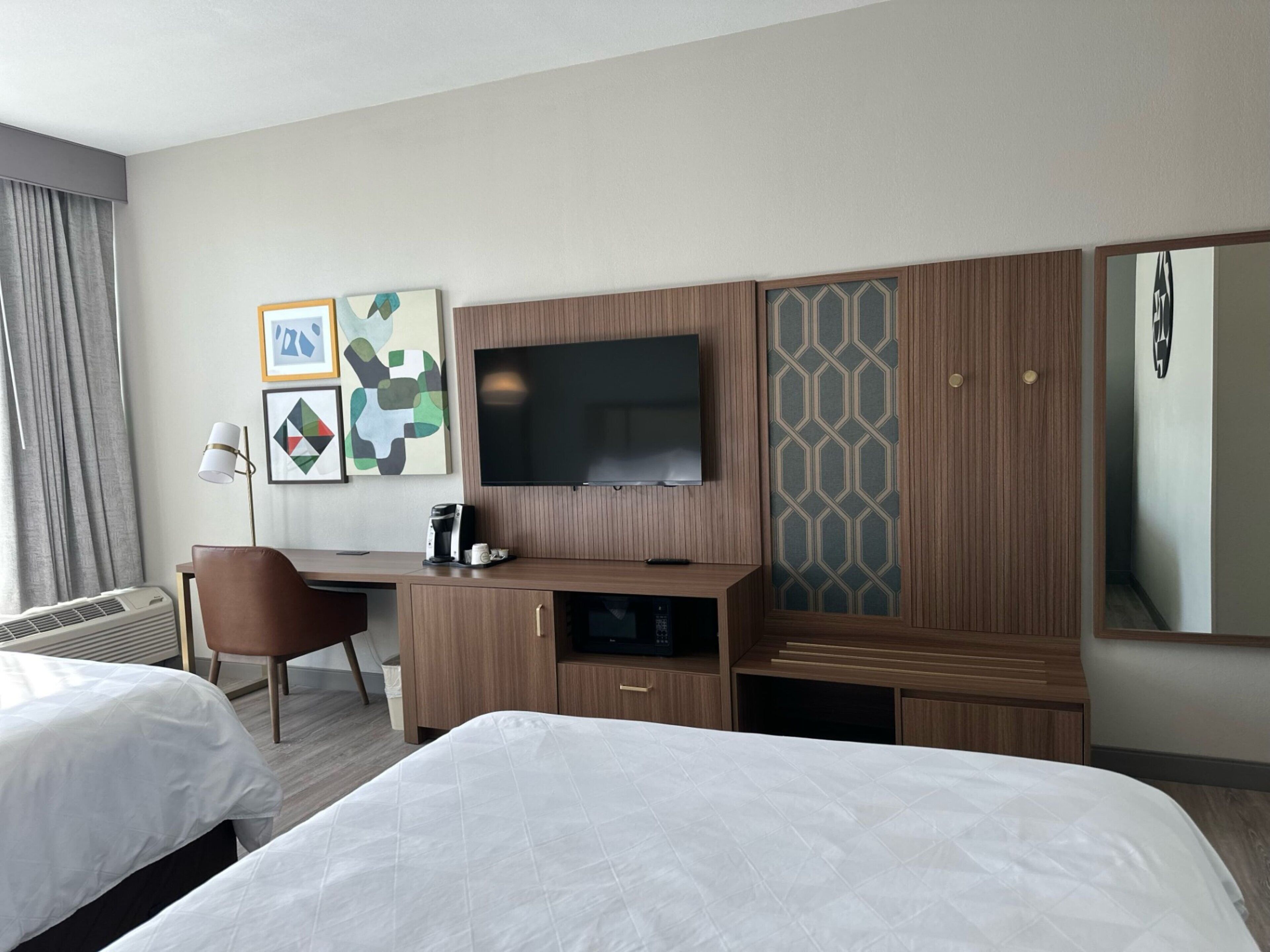 A hotel room with two beds, a desk with a flat-screen TV, a coffee maker, and artwork on the wall.