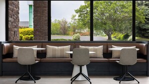 A modern seating area with a sofa and two chairs, a stone pillar, and a view of a green building and trees. - Holiday Inn Roanoke-Tanglewood-Rt 419&i581 by IHG (Roanoke)