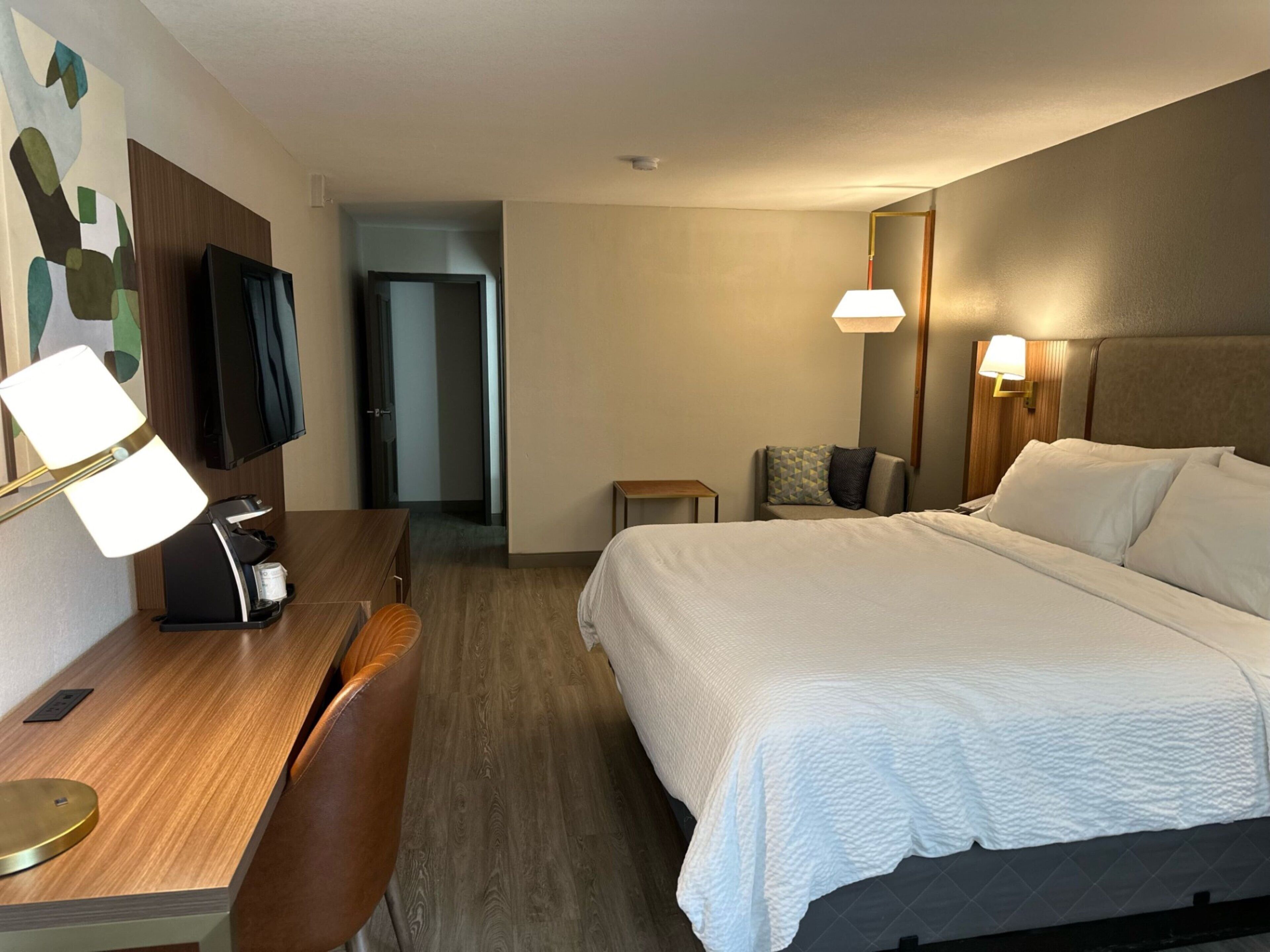A hotel room with a bed, desk, chair, television, and two bedside lamps.