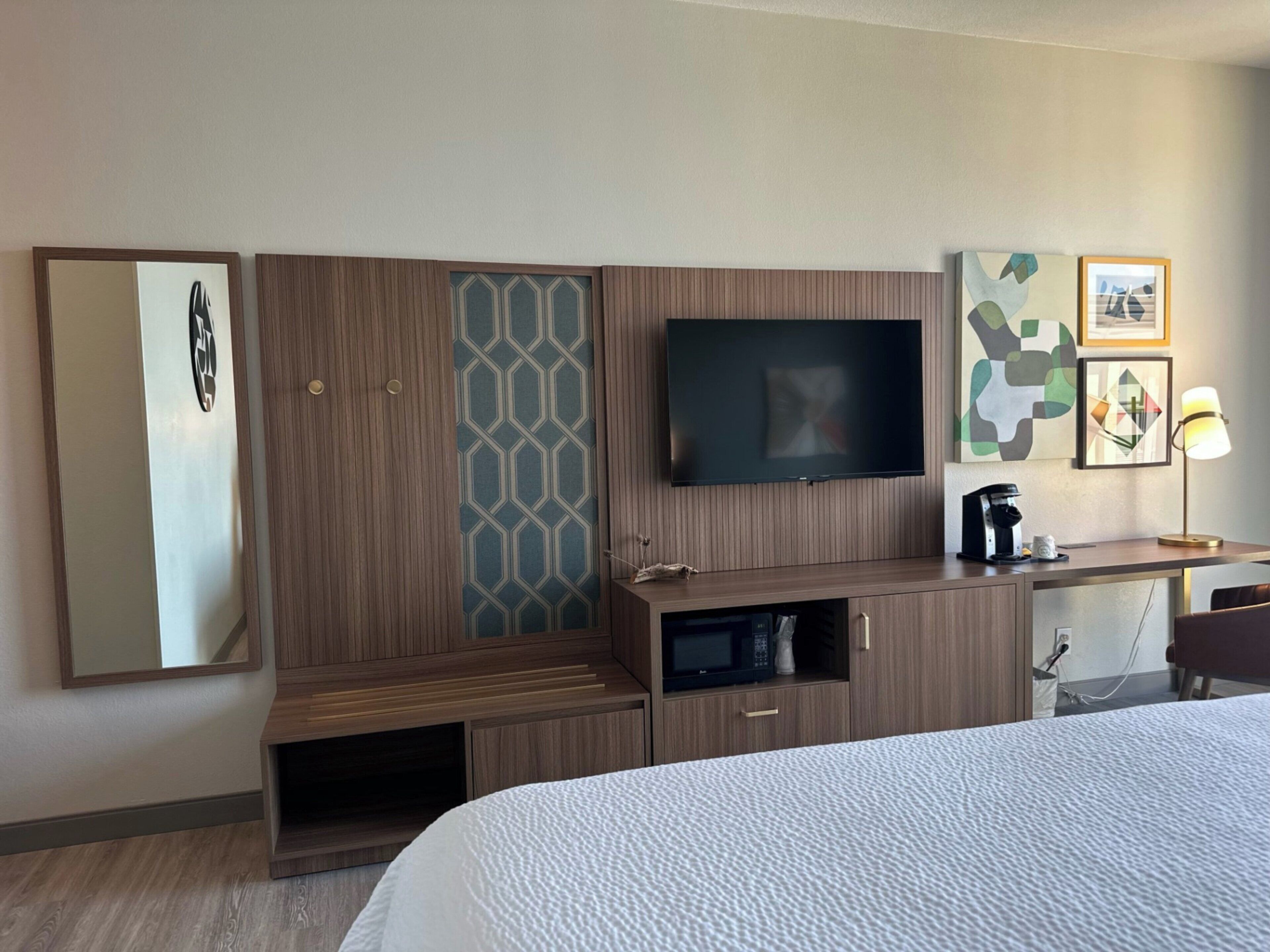 A hotel room with a bed, a TV, a desk with a lamp, and a coffee maker.