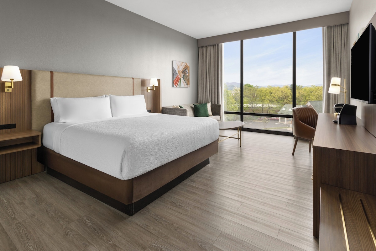 A modern hotel room with a large bed, a desk, and a chair.