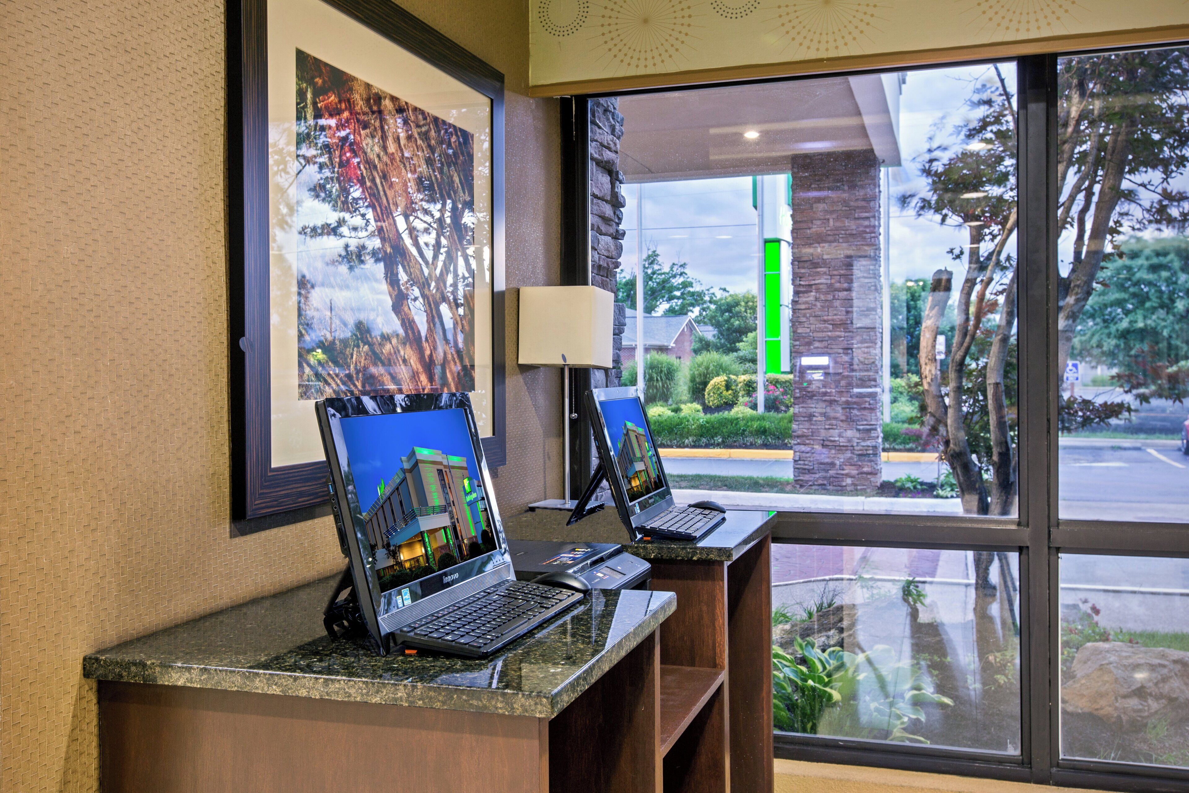 Una recepción de hotel con dos computadoras portátiles, un cuadro en la pared y vistas al exterior a través de una ventana.