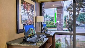 Una recepción de hotel con dos computadoras portátiles, un cuadro en la pared y vistas al exterior a través de una ventana.