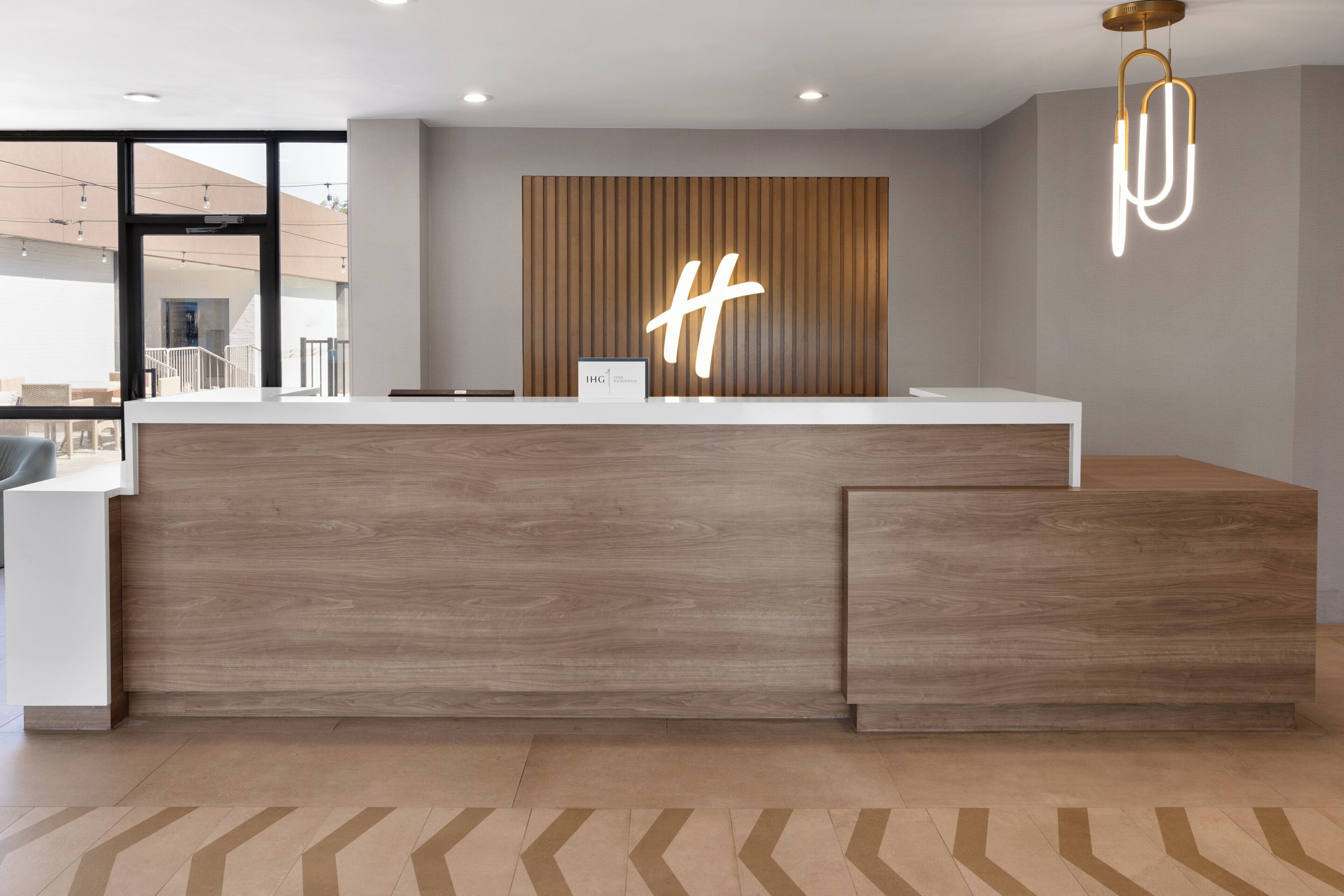 A reception desk with a wooden finish, a large illuminated 'H' sign, and a modern chandelier.