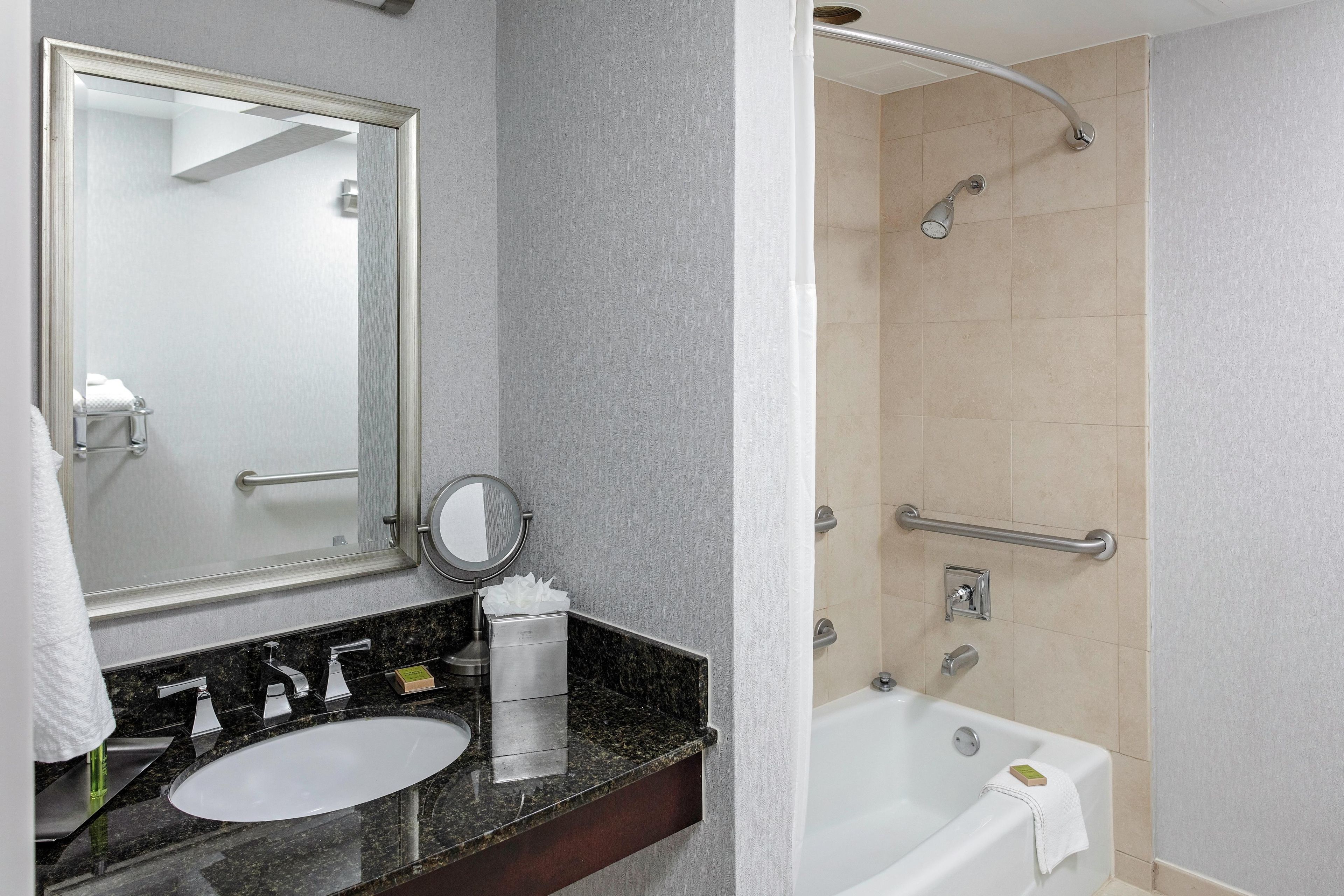 Un baño con lavamanos, espejo, toallero y ducha equipada con barras de apoyo.
