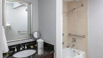 Un baño con lavamanos, espejo, toallero y ducha equipada con barras de apoyo.