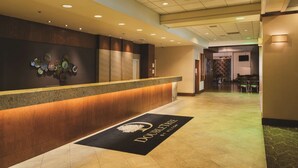 A hotel reception area with a wooden reception desk, a wall-mounted art display, and a black doormat with the hotel name. - DoubleTree by Hilton Omaha Downtown (Omaha)