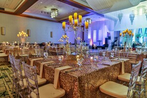 A banquet hall with tables covered in gold sequined tablecloths, clear chairs, and ornate chandeliers. - DoubleTree by Hilton Omaha Downtown (Omaha)