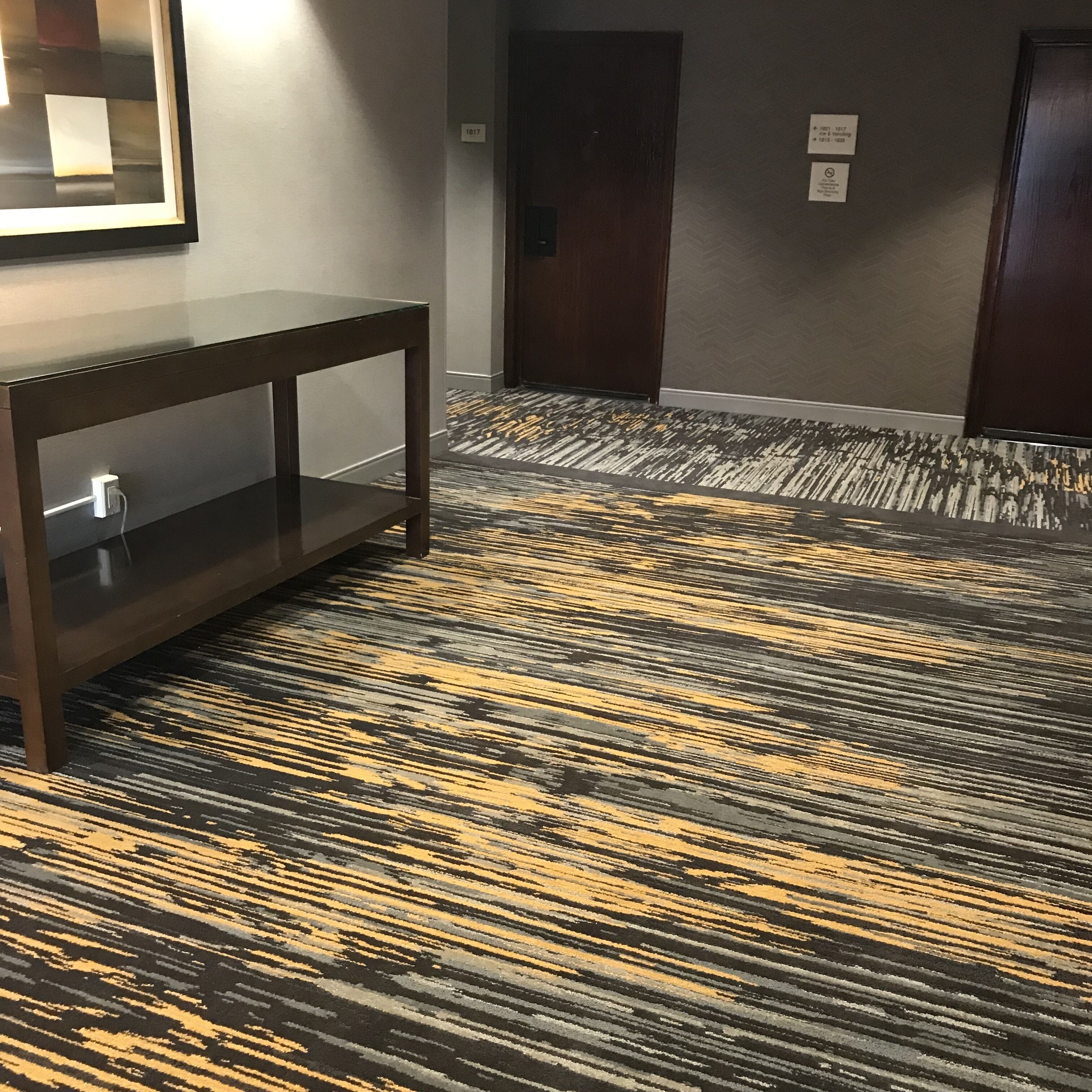 A hallway with a patterned carpet, a console table, and two doors.