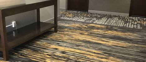 A hallway with a patterned carpet, a console table, and two doors.