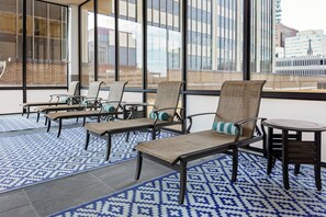 A modern indoor seating area with wicker chairs and a small table, large windows with a city view, and patterned floor mats. - DoubleTree by Hilton Omaha Downtown (Omaha)