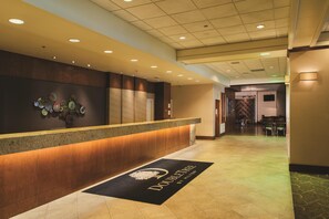 A hotel reception area with a wooden reception desk, a wall-mounted art piece, and a doormat with the hotel's name. - DoubleTree by Hilton Omaha Downtown (Omaha)