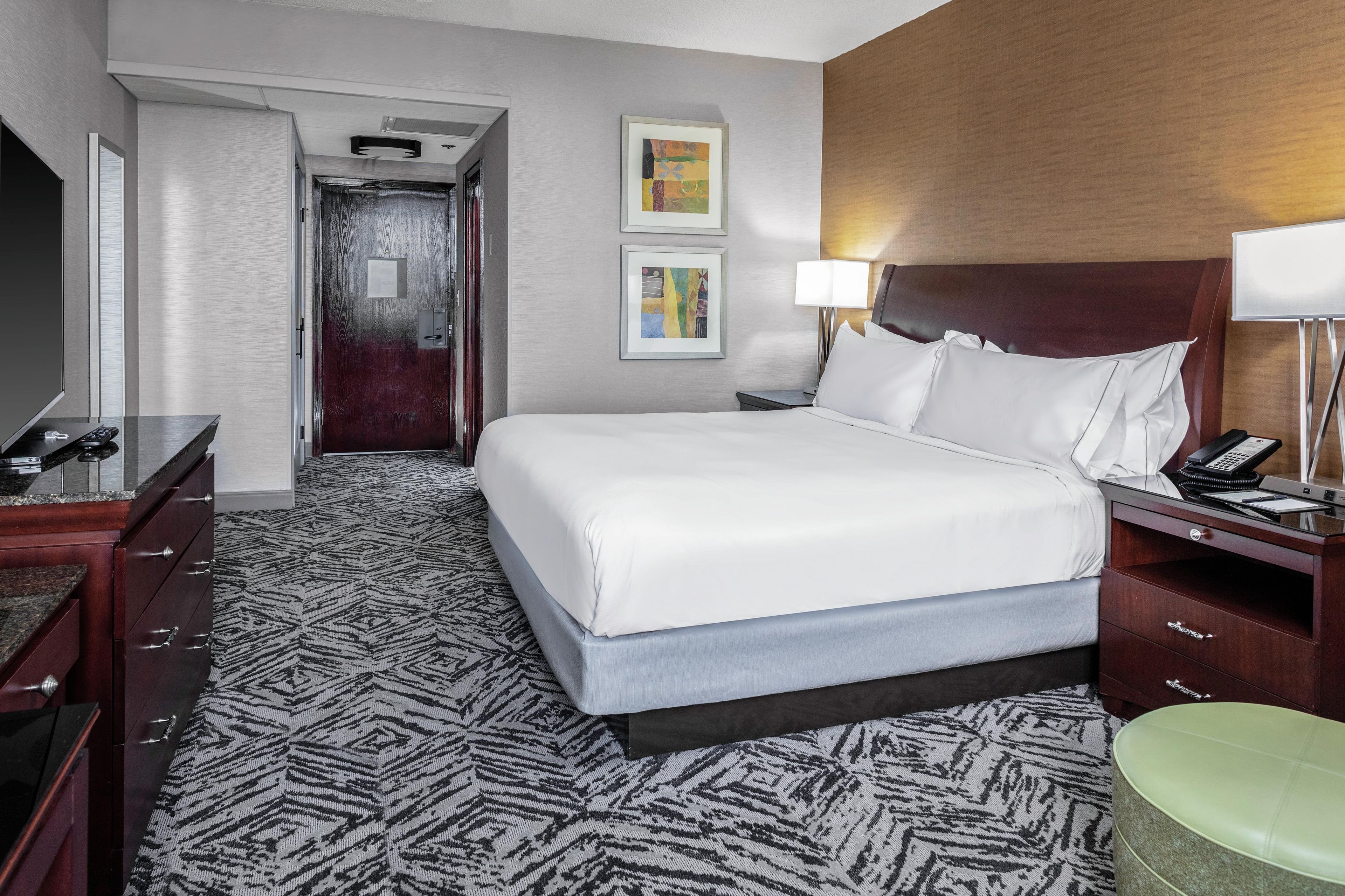 A hotel room with a bed, bedside table, lamp, and a desk with a telephone.