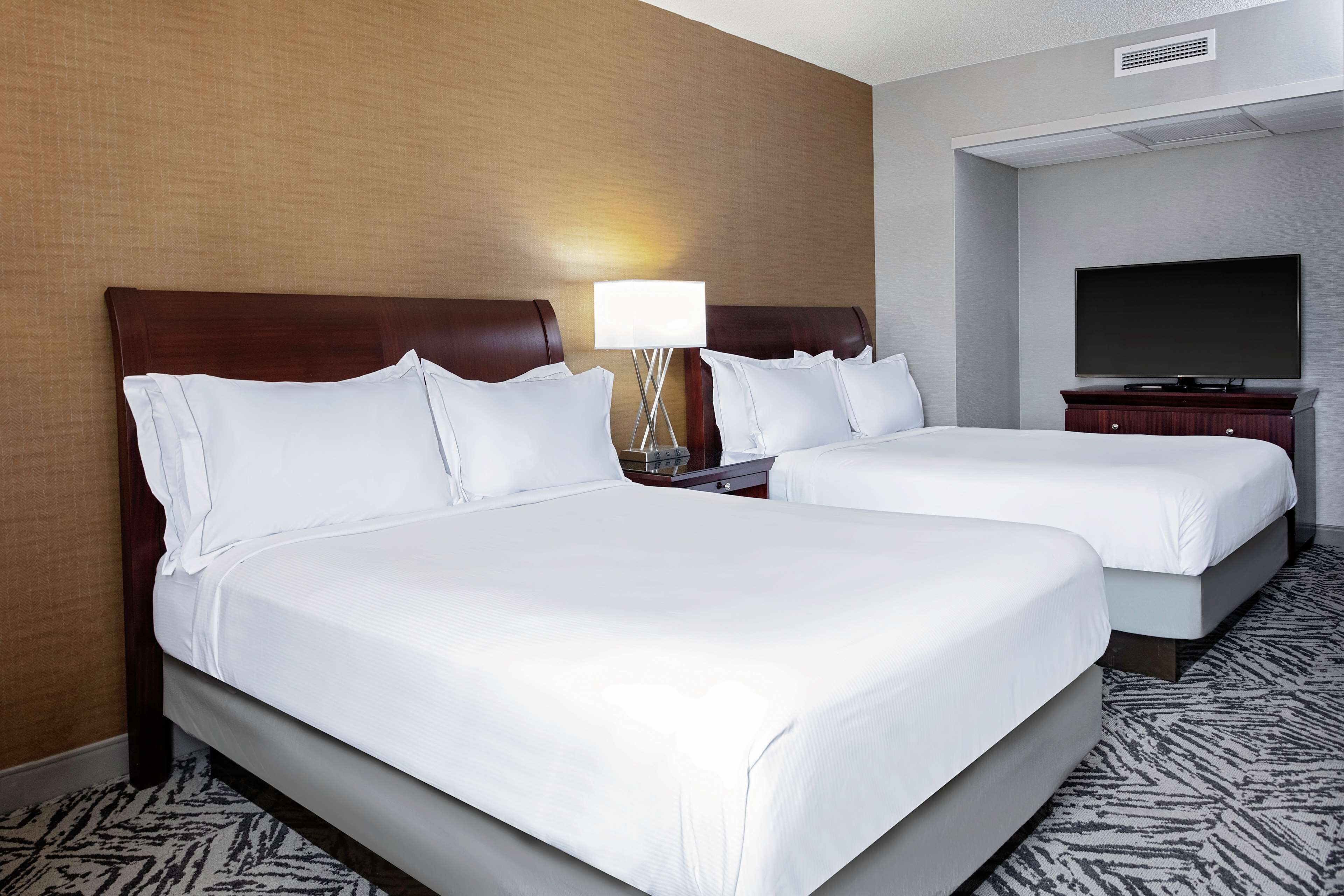 A hotel room with two beds, a TV, and a lamp.