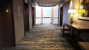 A hotel corridor with a patterned carpet, wooden doors, and a bench with a lamp.