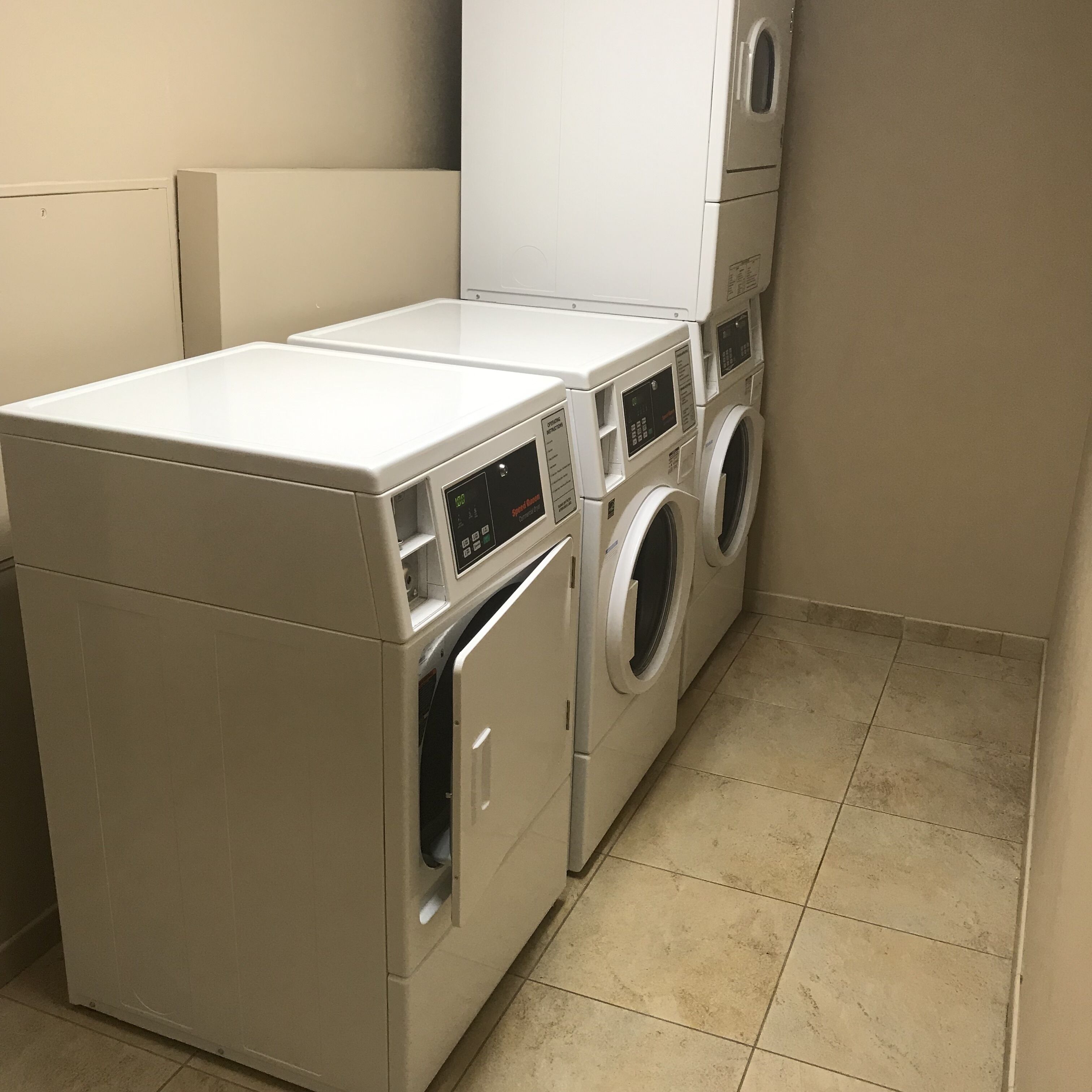 A laundry room with a front-loading washer and dryer, a white cabinet, and a tiled floor.