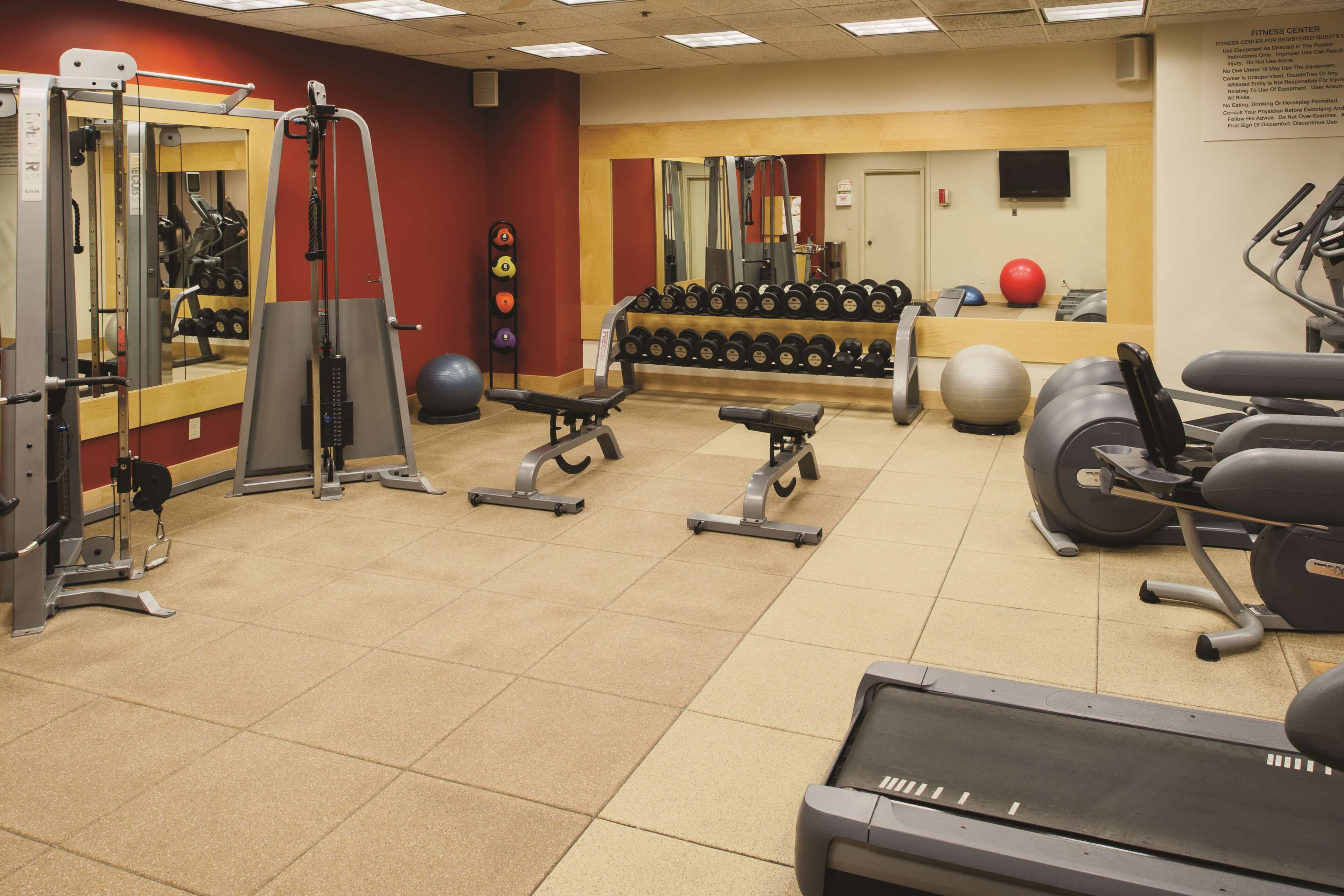 Un gimnasio con diverso equipo de ejercicio, que incluye cintas de correr, máquinas de pesas y pesas sueltas.
