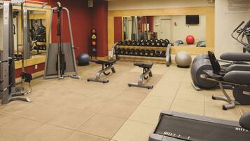 Un gimnasio con diverso equipo de ejercicio, que incluye cintas de correr, máquinas de pesas y pesas sueltas.