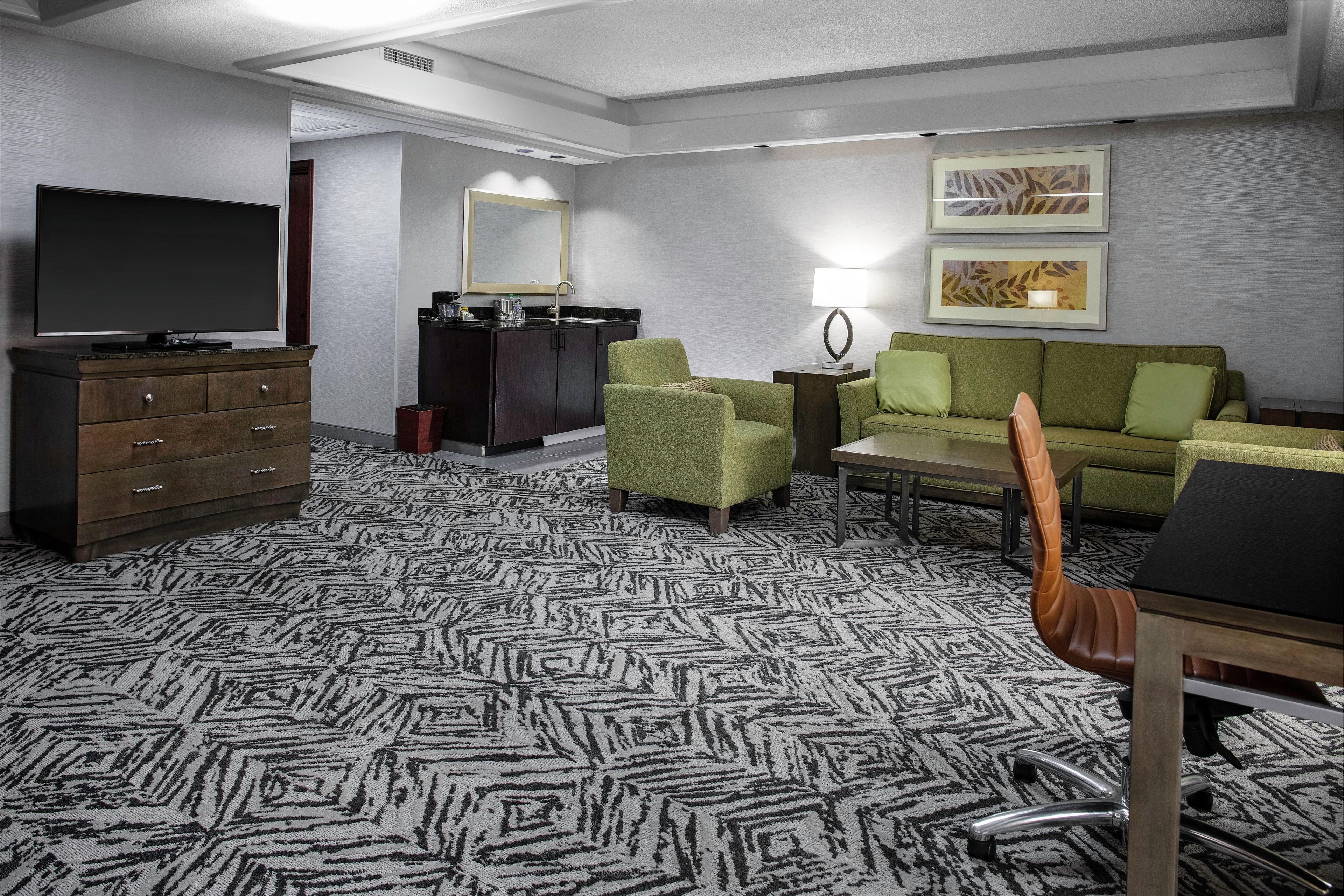 Une chambre d’hôtel équipée d’un téléviseur à écran plat, d’une commode, d’un canapé, d’une table basse, d’une lampe et d’un sol recouvert de moquette.