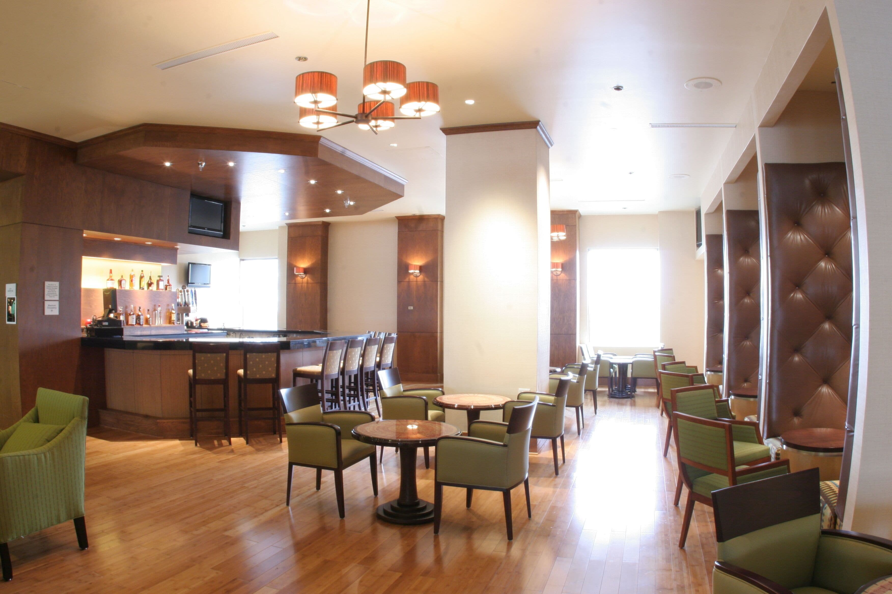A hotel lobby with a bar area, multiple seating arrangements, and a television mounted on the wall.