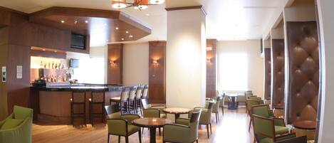 A hotel lobby with a bar area, multiple seating arrangements, and a television mounted on the wall.
