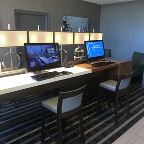 A hotel workspace with two desks, each with a computer monitor, keyboard, and mouse. There are two chairs at each desk. The room has a patterned carpet and a wall with a textured design. - DoubleTree by Hilton Omaha Downtown (Omaha)