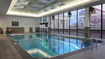 Una piscina interior con agua cristalina, suelo de baldosas y vistas a edificios a través de amplias ventanas.