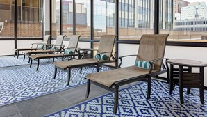 A modern outdoor seating area with wicker chairs and a small round table, featuring a patterned blue and white rug and large windows offering a city view. - DoubleTree by Hilton Omaha Downtown (Omaha)