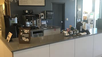 Un comptoir de café avec des machines à expresso, un tableau affichant le menu et une poubelle.