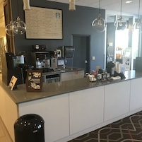 Un comptoir de café avec des machines à expresso, un tableau affichant le menu et une poubelle.