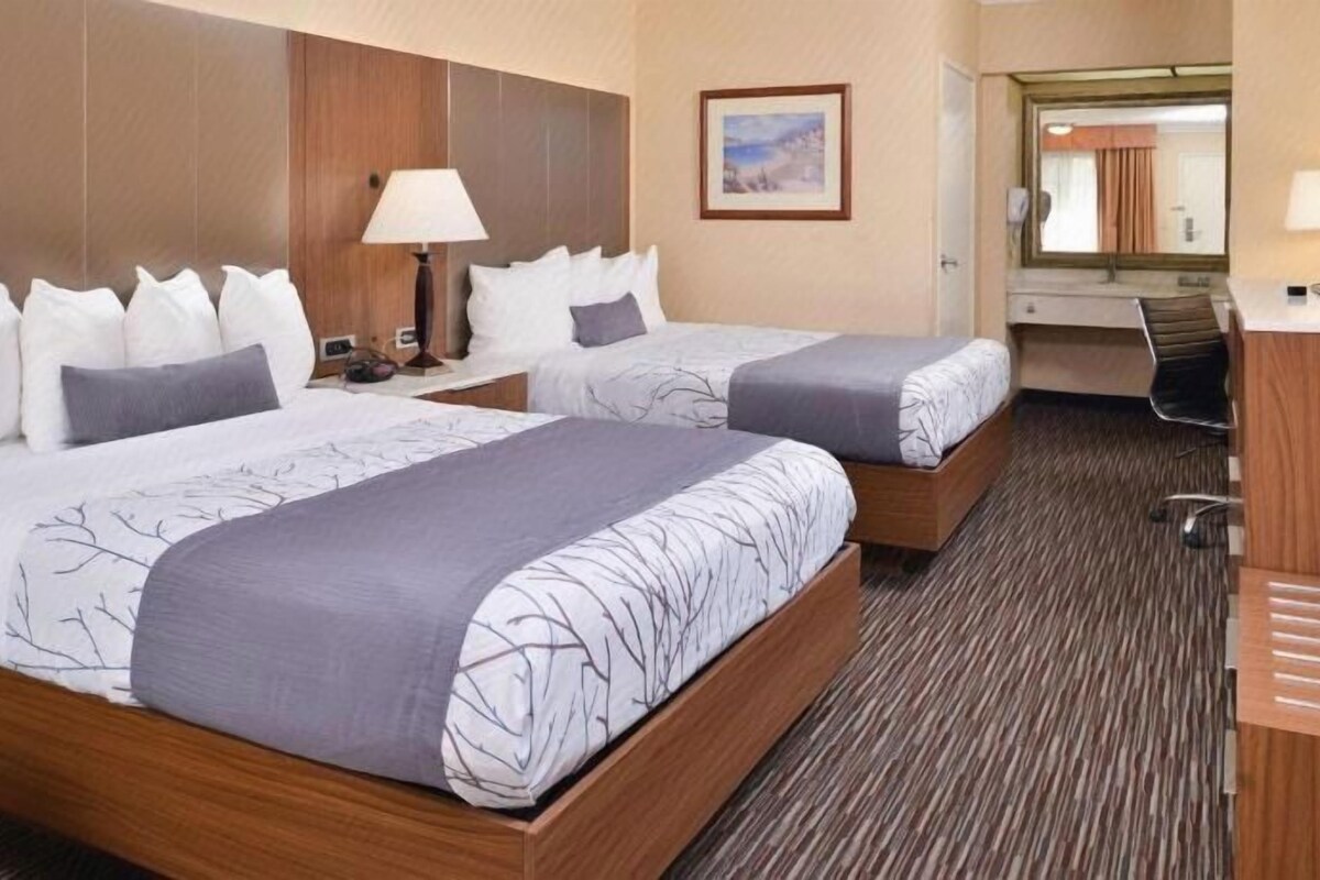 A hotel room with two beds, a desk, a chair, a lamp, and a mirror.