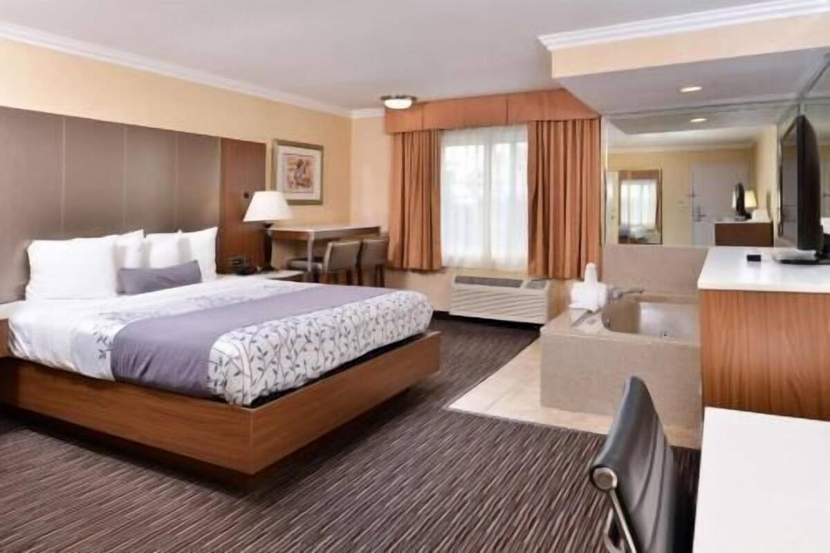 A hotel room with a large bed, a desk, a chair, a bathroom with a bathtub, and a mirror.