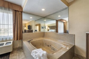 A modern bathroom with a large freestanding bathtub, a mirror, and a window with curtains.