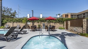 A swimming pool with lounge chairs and red umbrellas, surrounded by stone walls and greenery. - Best Western Airpark Hotel - LAX Airport LA  Stadium (Inglewood)