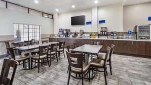 A restaurant with multiple tables and chairs, a counter with various food items, and a television mounted on the wall. - Best Western Airpark Hotel - LAX Airport LA  Stadium (Inglewood)