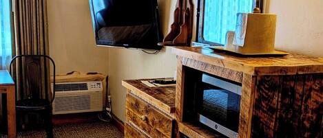 A hotel room with a wooden dresser, a flat-screen TV, a microwave, and a small refrigerator.