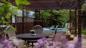 A wooden deck with a round table and chairs, a hot tub, and a wooden fence. - Browns Canyon Inn (Salida)