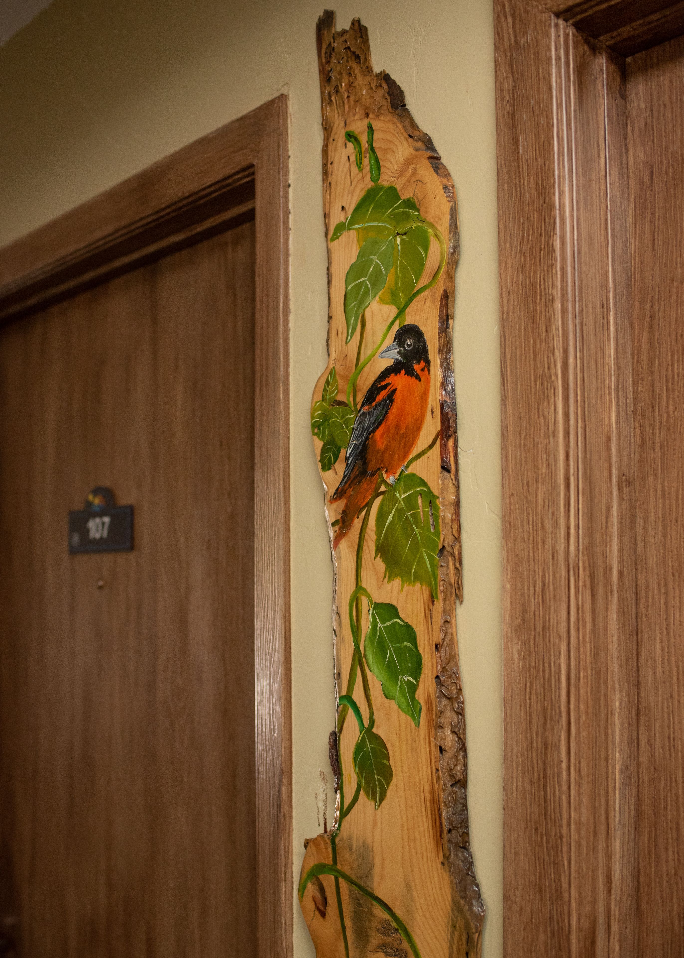 A wooden wall art of a bird with green leaves.