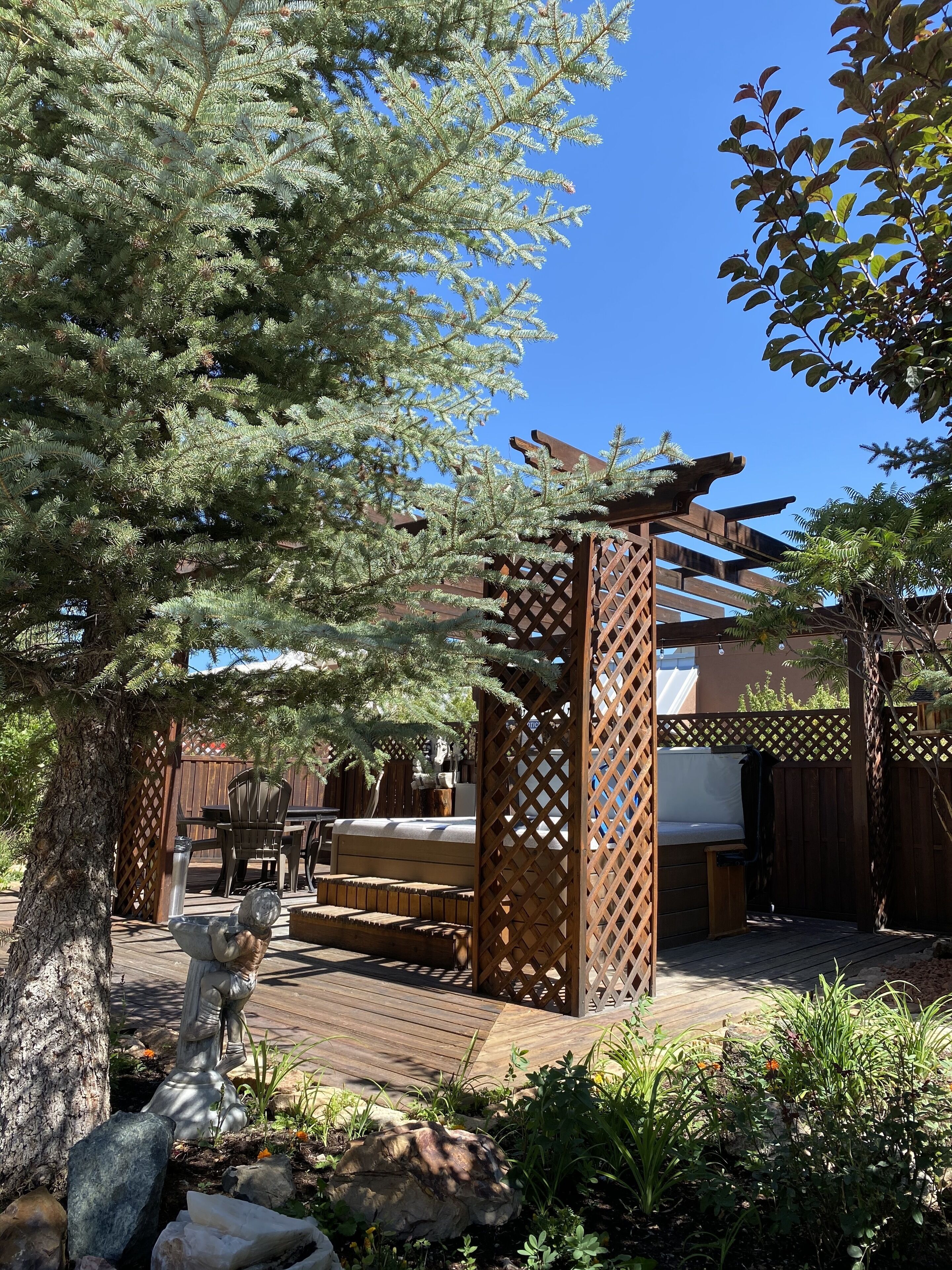 Una terraza de madera con mobiliario exterior, un pérgola y una estatua.