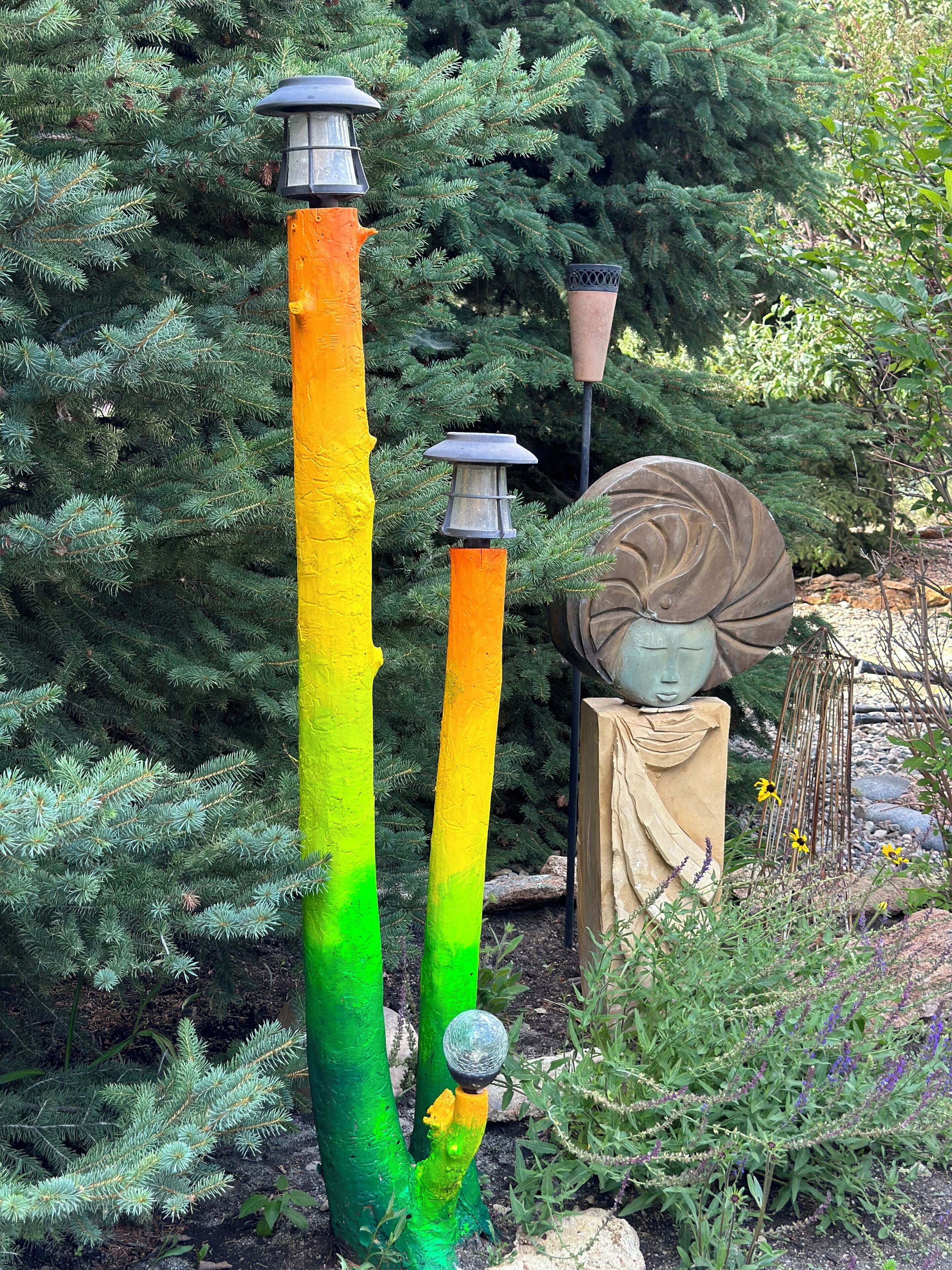 A garden with a tall, colorful pole, a birdhouse, and a statue.