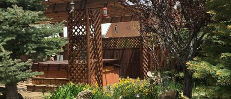 A wooden pergola structure with a lattice design, surrounded by a garden with various plants and rocks.