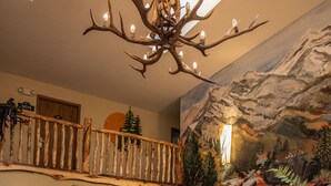 A rustic interior with a chandelier, wooden furniture, and a mural of a mountain landscape. - Browns Canyon Inn (Salida)