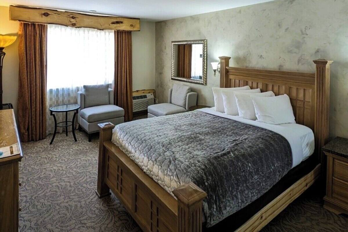 A hotel room with a large bed, a small table, a chair, a mirror, and a window with curtains.